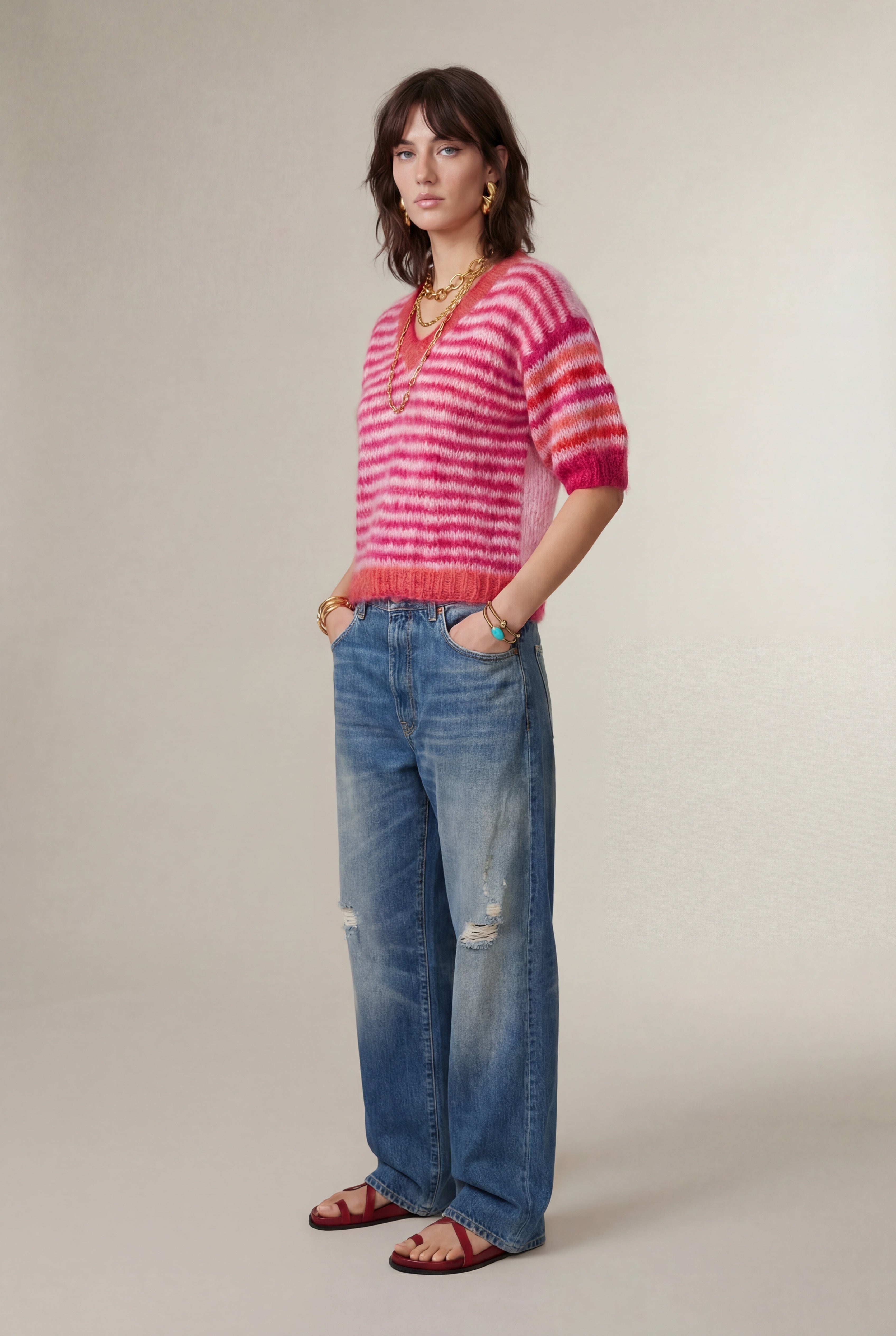 Woman wearing a pink and red striped sweater and blue jeans against a plain background