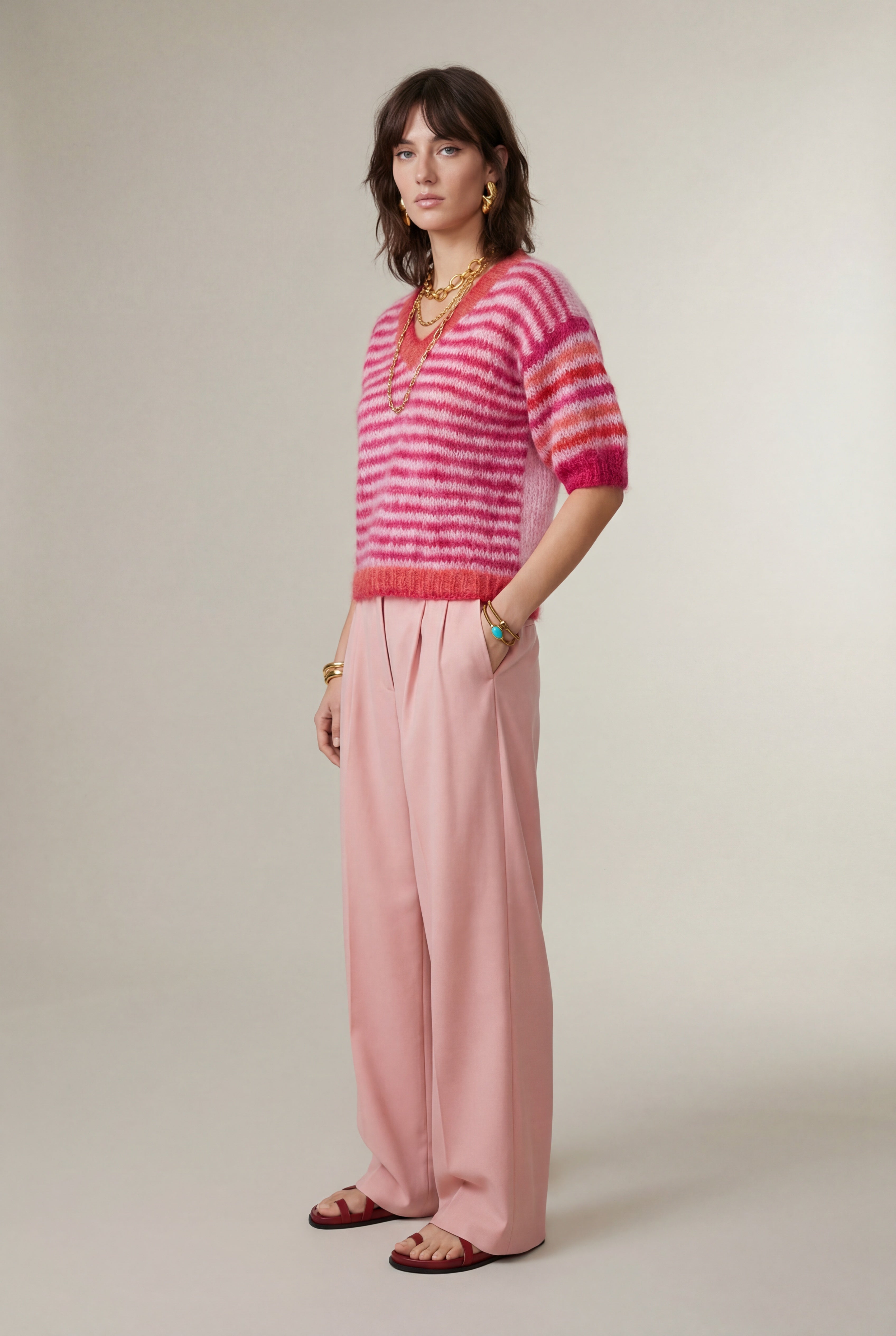 Woman wearing a pink and red striped sweater with pink pants on a plain background