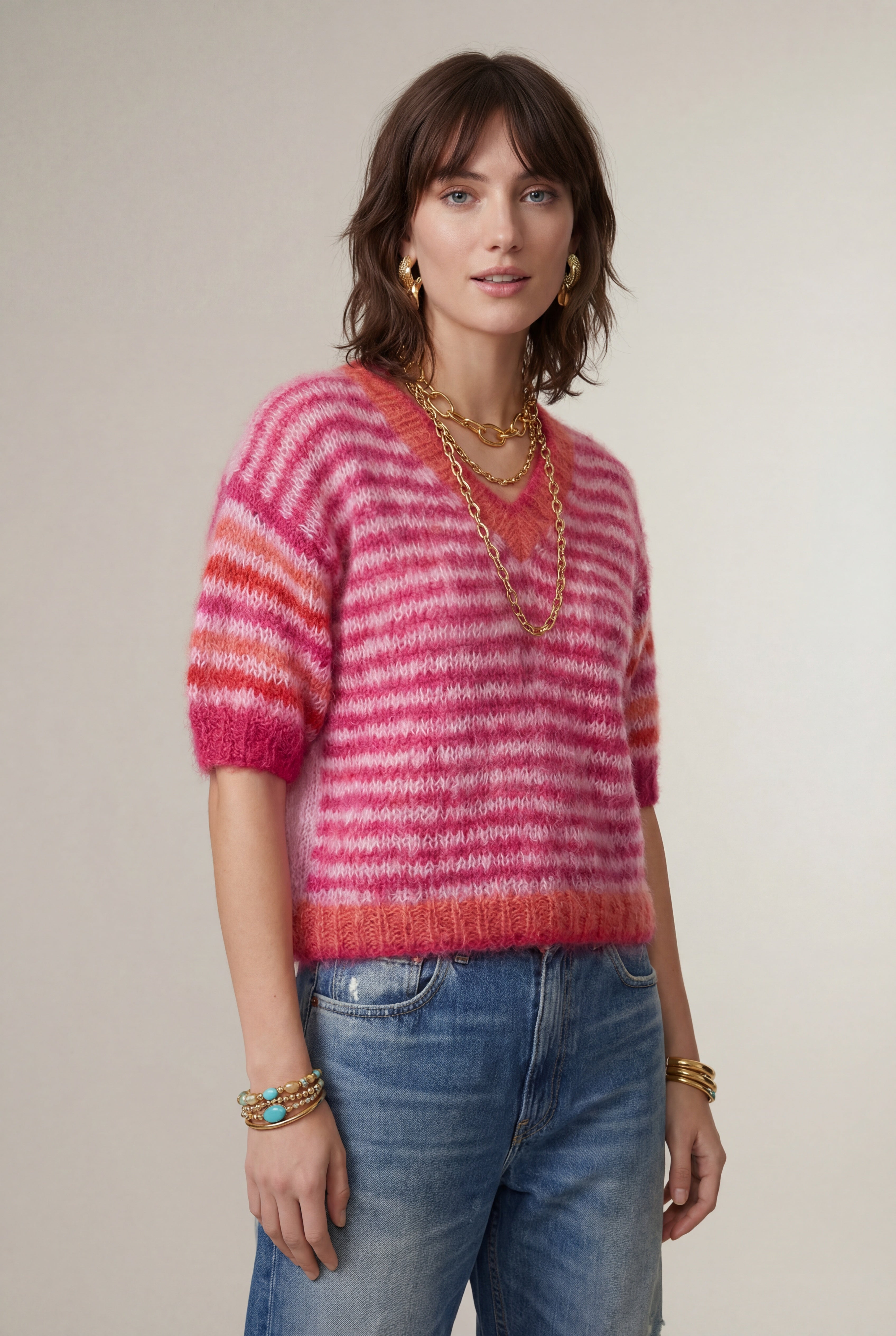 Woman wearing a pink and red striped sweater with blue jeans against a plain background
