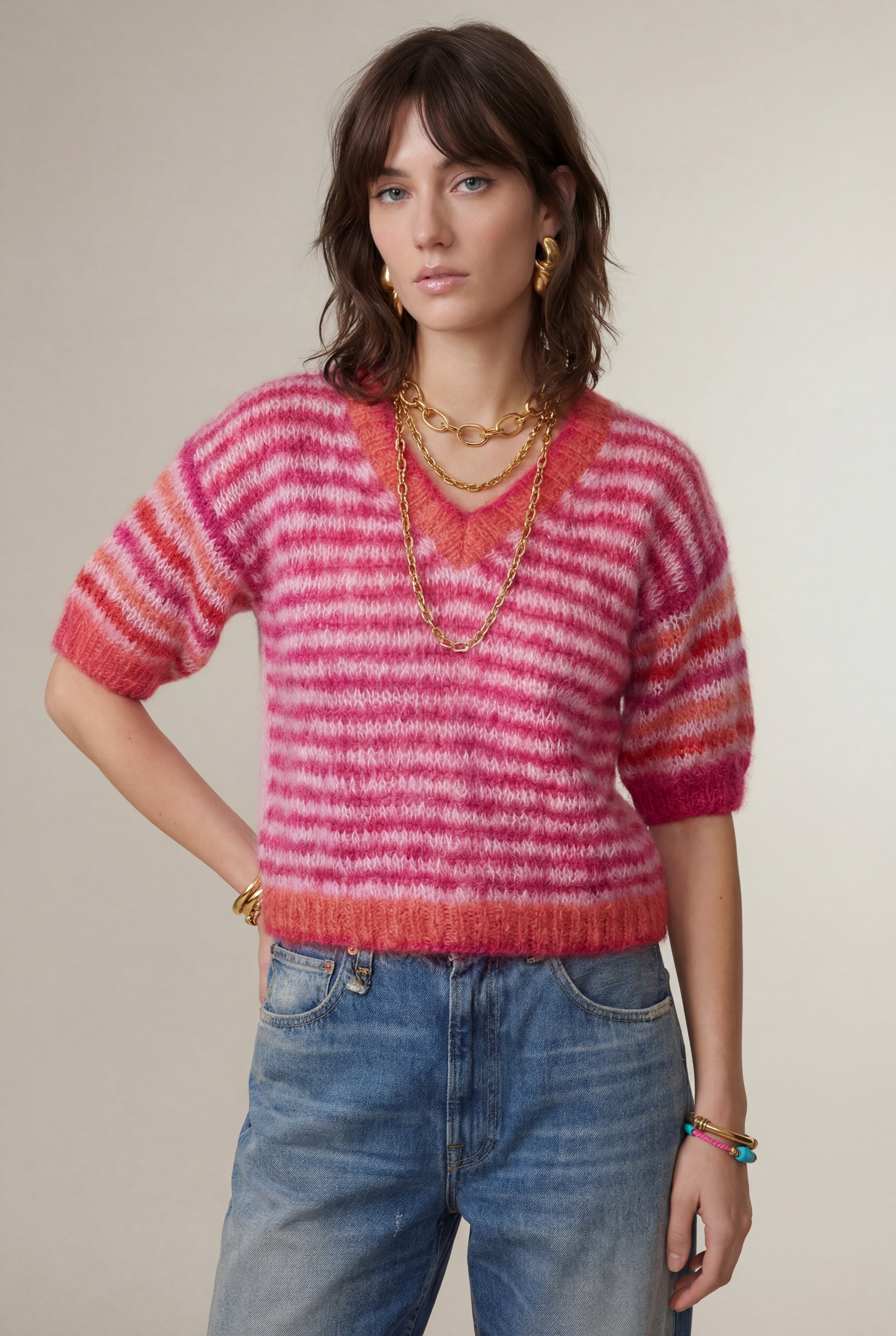 Woman wearing a pink and red striped sweater with blue jeans against a neutral background